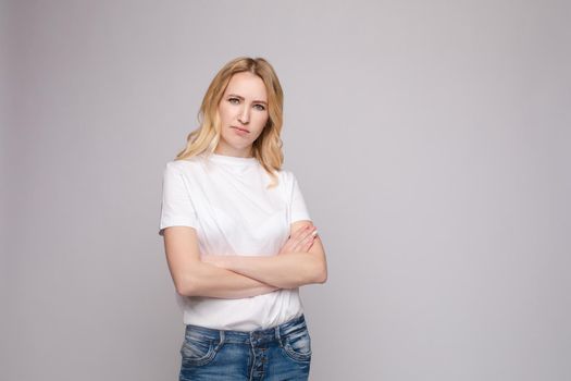 Studio portrait of unsatisfied young brunette caucasian woman with wavy hair in overall with colorful pattern holding arms folded and looking at camera with grief, dissatisfaction, anger and disbelief. Isolate.