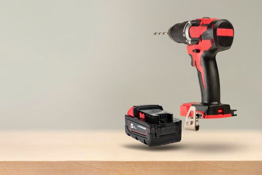 Wireless tools. Cordless drill with drill bit. The screwdriver with the battery removed falls, casting a shadow. Advertising banner of construction or industrial theme on wooden background.