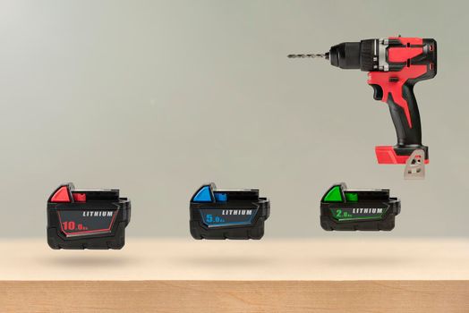 Batteries for cordless tools. Batteries for a screwdriver of different capacities and different sizes. Electric drill and three batteries with a charge indicator on a wooden background.