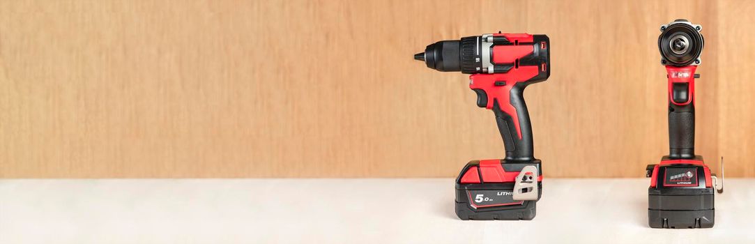 Cordless drill in black and red. A screwdriver with a drill lies on a wooden background. Modern carpentry tool close-up