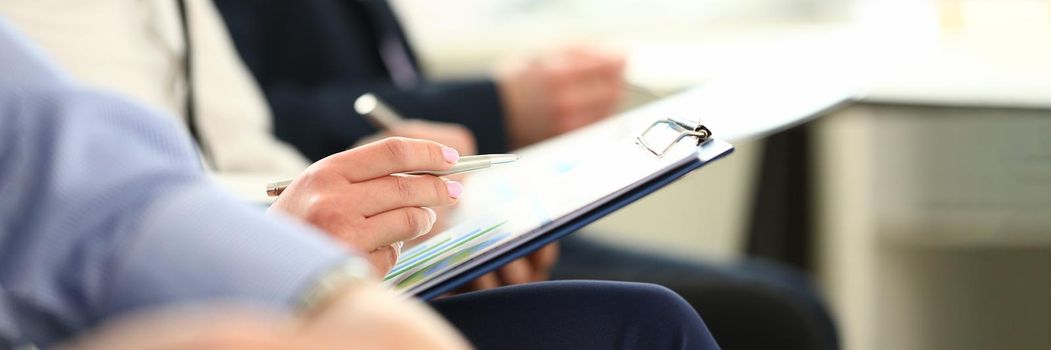 Focus on male hands holding paper folder with important agreements and writing something. Colleagues at biz seminar. Company meeting concept. Blurred background