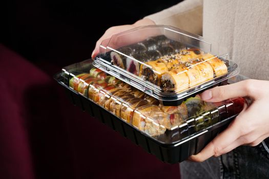 Sushi roll food delivery service. Holding sushi set box on black background. Traditional Japanese seafood. Delicious roll.