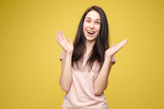 Front view of surprised young girl in bright dress looking at camera on yellow isolated background in studio. Funny amazed female with open eyes shouting. Concept of shock and happiness.