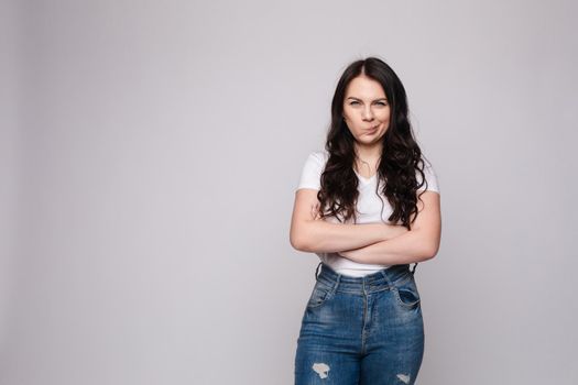 Studio portrait of unsatisfied young brunette caucasian woman with wavy hair in overall with colorful pattern holding arms folded and looking at camera with grief, dissatisfaction, anger and disbelief. Isolate.