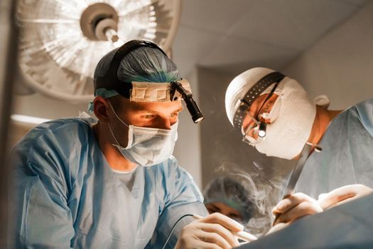 2 surgeons with headlamp do plastic operation in medical clinic. Chest augmentation plastic operation and correction in medical clinic