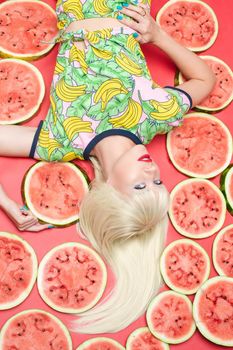 View from above fashionable blonde with makeup lying near fresh tasty watermelon. Attractive female model looking at camera and posing with sweet fruits. Concept of summer and brightness.