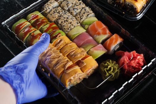 Sushi roll food delivery service at quarantine covid-19 period. Holding sushi set box using medical gloves on black background