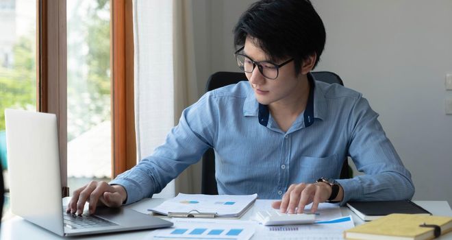 Portrait of Young Asian man hand freelancer is working her job on computer tablet in modern office. Doing accounting analysis report real estate investment data, Financial and tax systems concept..