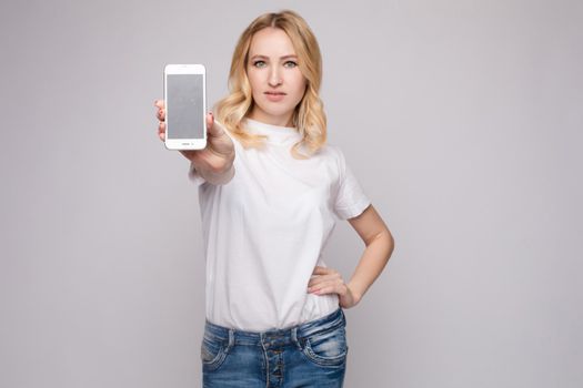 Studio portrait of beautiful caucasian brunette woman in patterned overall pointing at her smartphone with index finger. She is certain or sure about something. I know gesture.