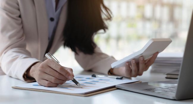 Close-up of a businesswoman hand holding a pen pointing at a graph with a calculator glasses laptop placed at the office..