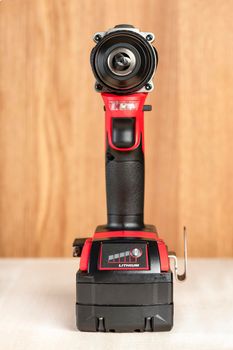 Cordless drill in black and red. A screwdriver with a drill lies on a wooden background. Modern carpentry tool close-up