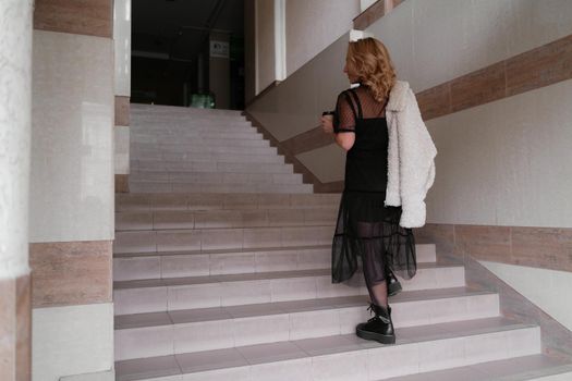 Portrait of a beautiful smiling blonde. She's walking up the stairs, coffee in hand. The Concept Of Urban Life