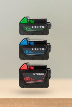 Batteries for cordless tools. Batteries for a screwdriver of different capacities and different sizes. Electric drill and three batteries with a charge indicator on a wooden background.