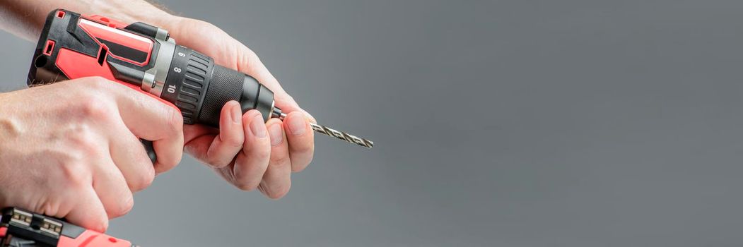 The man's hands install the drill into the drill, the hands take the drill and install it into the electric drill. Cordless tool on a gray background