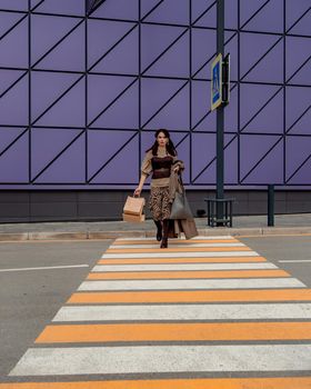 A beautiful girl with shopping bags is walking along a pedestrian crosswalk. Consumerism, shopping, shopping, lifestyle concept.