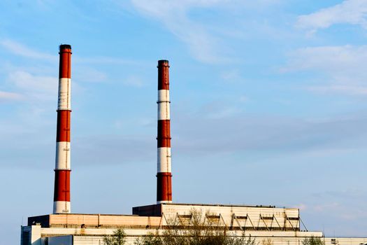 a building or group of buildings where goods are manufactured or assembled chiefly by machine.Two factory pipes of a thermal power plant against the blue sky.