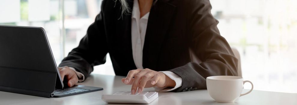 Business woman using calculator and writing make note with calculate. Woman working at office with laptop and documents on his desk.