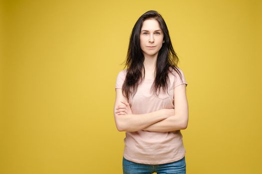 Studio portrait of fashionable brunette lady in white dress with flowers and beige heels posing with bent leg. Smiling at camera. holding skirt. Isolate on yellow background.