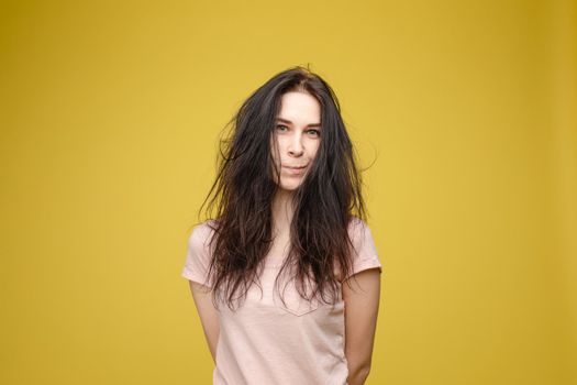 Pretty blonde haired woman wearing in black sweater, holding messy unbrushed hair in one hand and pink hairbrush in another one. A frustrated girl looks at her hair on a white studio background.