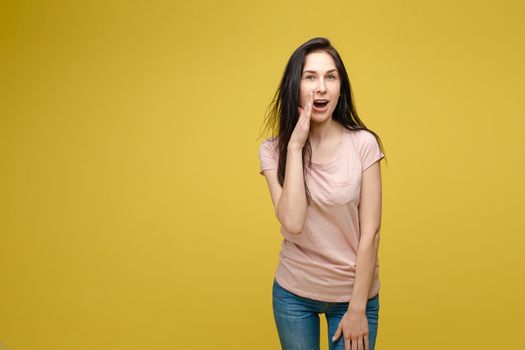 Studio portrait of curious brunette girl in multicolored top listening to the news or gossips with her ear.