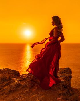 A woman is standing in a long red dress, a fashion model in an evening dress, soaring over the sea.
