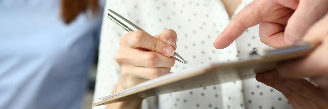 Close-up of smart people working in big modern office with smart manager. Trendy woman in classy blouse writing something in paper folder. Company meeting concept