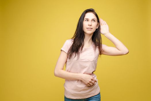 Studio portrait of curious brunette girl in multicolored top listening to the news or gossips with her ear.