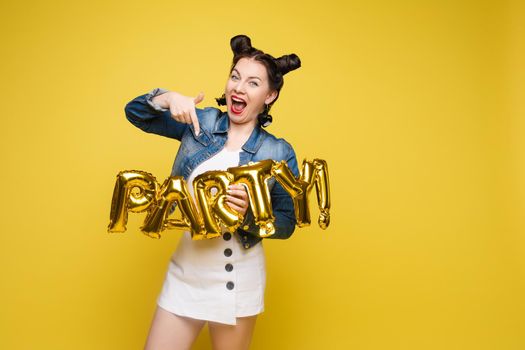 Attractive happy woman laughing holding big gold letters posing at yellow studio background medium long shot. Beautiful fashionable young girl relaxing having positive emotion