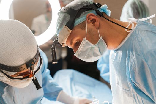 2 surgeons with headlamp do plastic operation in medical clinic. Chest augmentation plastic operation and correction in medical clinic