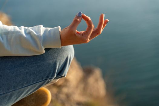 yoga, gesture and healthy lifestyle concept - hand of meditating yogi woman showing gyan mudra over sea sunset background.