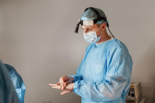 Surgeon with headlamp cleans his hands before plastic operation in medical clinic. Chest augmentation plastic operation and correction in medical clinic.