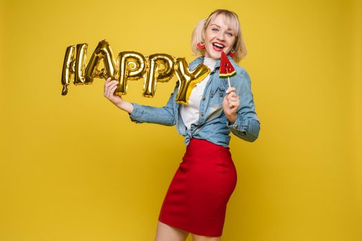 Attractive happy woman laughing holding big gold letters posing at yellow studio background medium long shot. Beautiful fashionable young girl relaxing having positive emotion