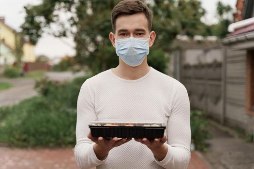 Sushi set in box healthy food delivery online service by car. Man courier in medical mask with sushi box stands in front of car