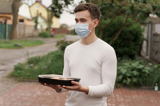 Sushi set in box healthy food delivery online service by car. Man courier in medical mask with sushi box stands in front of car