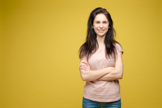 Studio portrait of fashionable brunette lady in white dress with flowers and beige heels posing with bent leg. Smiling at camera. holding skirt. Isolate on yellow background.