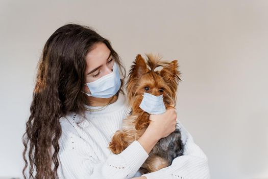 Young woman in medical mask hugs her dog yorkshire terrier wearing protective mask too