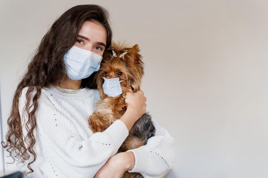 Young attractive woman with dog yorkshire terrier, both wearing protective mask on a white background. Health care and pet care. People and pets.