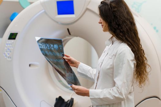 Medical student looks at x-ray picture of patient brain near kt komputer tomograhphy. Young girl in medical clinic gotes new expirience