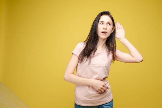 Studio portrait of curious brunette girl in multicolored top listening to the news or gossips with her ear.