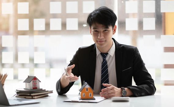 Miniature house in the hands of an Asian bussinessman real estate agent home loan working at the office. Looking at the camera..