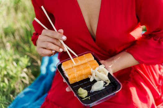 Close-up sushi set. Attractive girl holds sushi with chopsticks in hands. Courier delivered sushi set for pretty woman. Black box with sushi, wasabi, ginger.