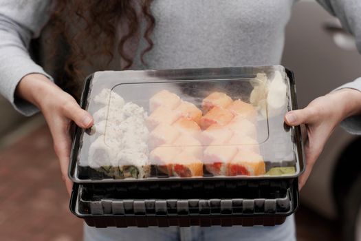 Close-up sushi in box healthy food delivery online service. Girl holds 2 sushi sets in hands. Japanese cuisine: rolls, soy sauce, wasabi.