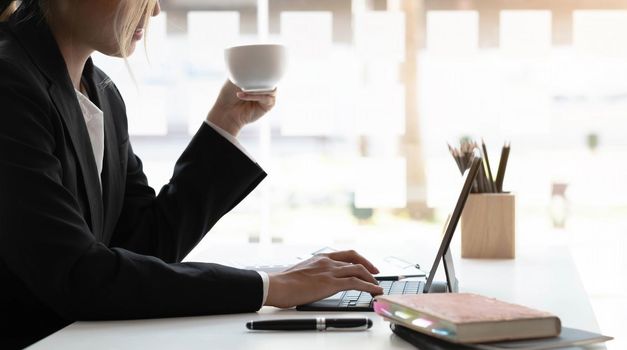 Smiling Asian businesswoman holding a coffee mug and laptop at the office. .