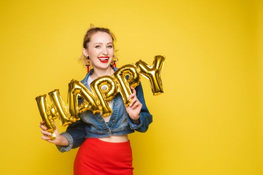 Stock photo portrait of attractive girl with red lips holding shining bright inflatable word HAPPY. Isolate on orange background.