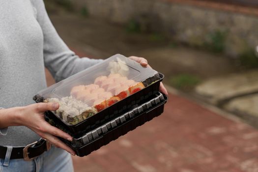 Close-up sushi in box healthy food delivery online service. Girl holds 2 sushi sets in hands. Japanese cuisine: rolls, soy sauce, wasabi