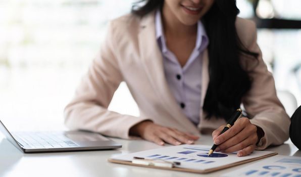 Businesswoman pointing pen at data graph, estimating profit and income statement of business in office..