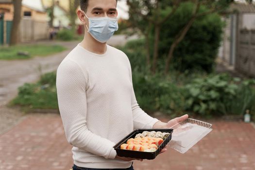 Sushi set in box healthy food delivery online service by car. Man courier in medical mask opens sushi box