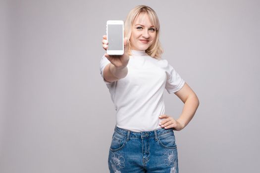 Studio portrait of beautiful caucasian brunette woman in patterned overall pointing at her smartphone with index finger. She is certain or sure about something. I know gesture.