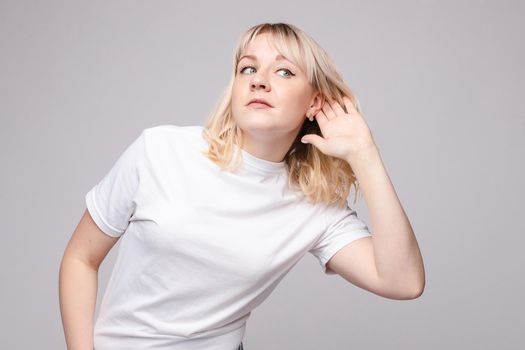 Studio portrait of curious brunette girl in multicolored top listening to the news or gossips with her ear.