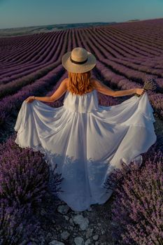 charming Young woman with a hat and white dress in a purple lavender field. LIfestyle outdoors. Back view.